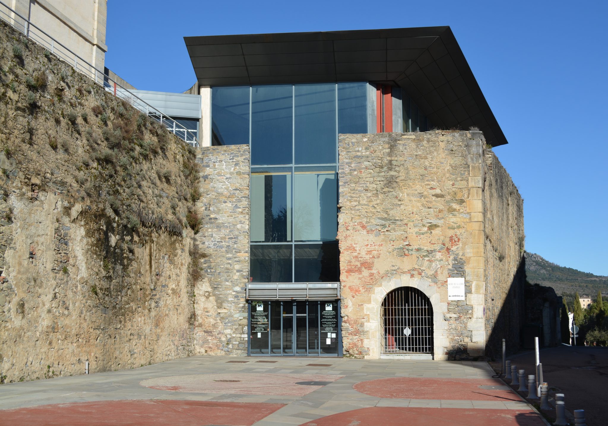 Photo montrant l'entrée du musée de la Corse, dont l'architecture mélange des menuiseries très moderne et l'ancienne citadelle avec ses remparts et ses murs en pierre